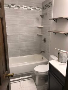 A renovated bathroom with a new tub/shower combo, toilet, and wall shelving by Prenga Remodeling in Orange, CT
