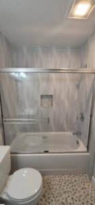 A renovated bathroom featuring a bathtub with a glass sliding door and wavy grey tiles by M J Services Home Remodeling in Gaithersburg, MD.
