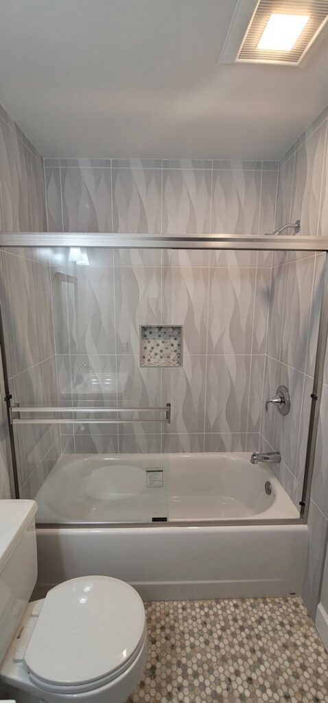 A renovated bathroom featuring a bathtub with a glass sliding door and wavy grey tiles by M J Services Home Remodeling in Gaithersburg, MD.