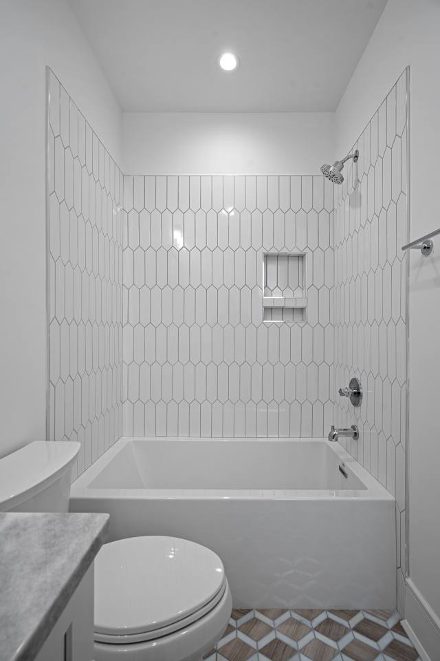 A clean bathroom with a white bathtub, toilet, and vertical subway tile shower surround installed by CML Builders in Charlotte, NC.