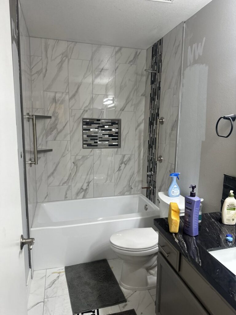 A newly renovated bathroom featuring a bathtub, toilet, and vanity with marble-look wall tiles by American Wolf Construction in Mesa, AZ