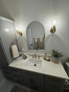 A newly installed bathroom vanity with dark gray cabinets, white countertop, and modern light fixtures by Branch Home Improvement LLC in Raleigh, NC.