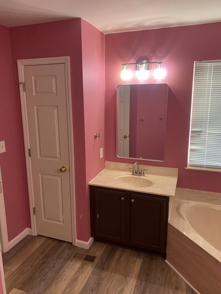 A bathroom with pink walls, new vanity, mirror, and light fixture, completed by Newhouse Construction St Louis in St. Louis, MO.