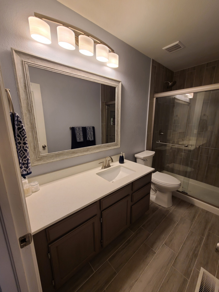 A renovated bathroom featuring a new vanity, mirror, and tiled shower by QCON LLC in Aurora, CO.
