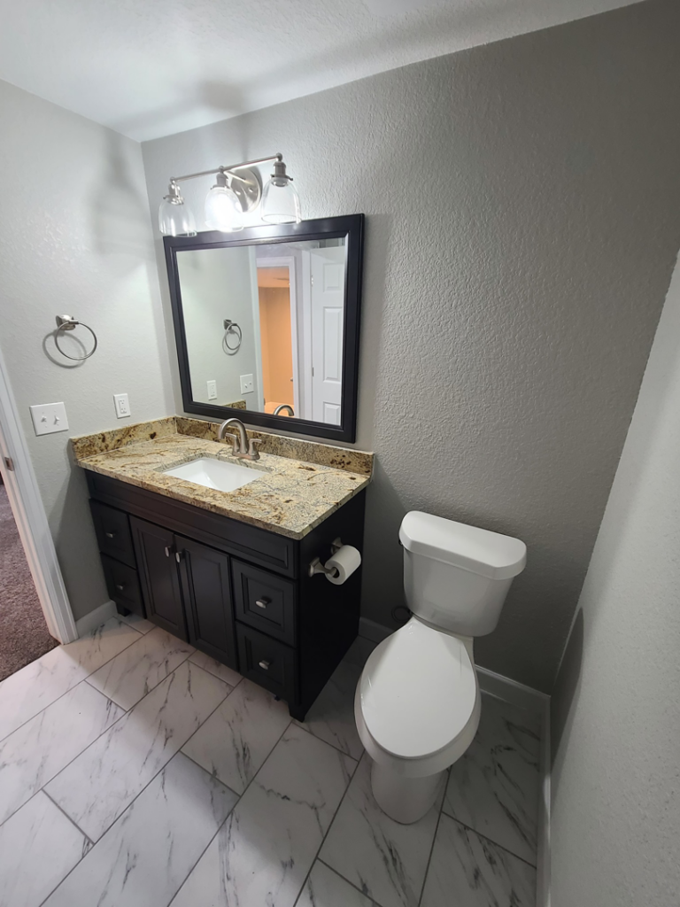 A renovated bathroom featuring a new vanity, sink, mirror, and tiled floor by QCON LLC in Aurora, CO.