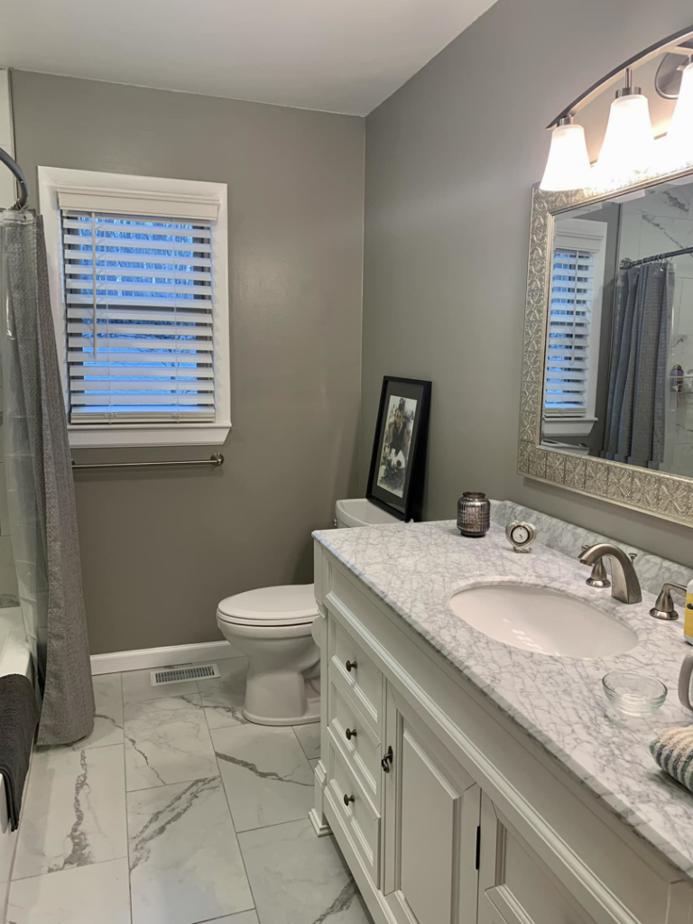 A renovated bathroom with a new vanity, mirror, and tile flooring by Heritage Design & Remodel in Raleigh, NC.