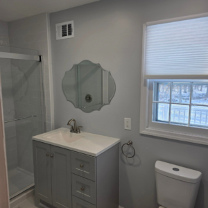 A renovated bathroom showing a modern vanity, mirror, and toilet installed by Noble Home Improvements in Edison, NJ.