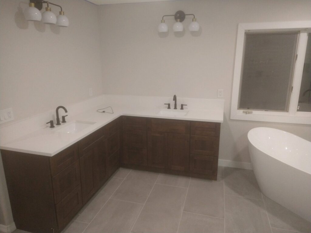 A newly renovated bathroom featuring a large L-shaped vanity with dual sinks and a modern freestanding tub by Mr. Affordable LLC in Denver, CO.