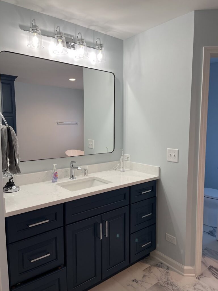 A renovated bathroom vanity featuring dark blue cabinets, a white countertop, and a large mirror by Synergy Builders in West Chicago, IL.