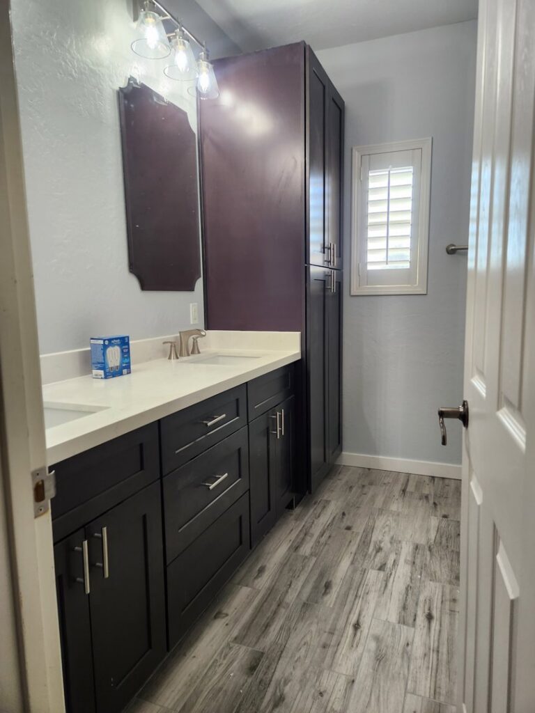 A bathroom with a new dark wood vanity, white countertop, and tall storage cabinet installed by LJ Builders in Chandler, AZ
