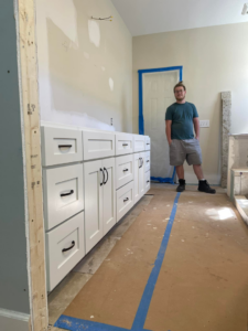 A handyman stands next to newly installed white base cabinets for a bathroom vanity by Wanderworks in Charleston, SC.