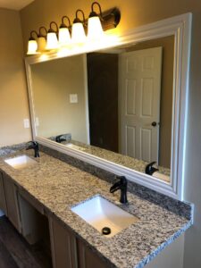 A renovated bathroom vanity with double sinks, granite countertops, and a large mirror with decorative lighting by MC Master Construction in League City, TX