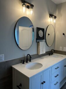 Newly installed bathroom vanity with double sinks, oval mirrors, and modern light fixtures by Supreme Tile & Flooring in Charlotte, NC.