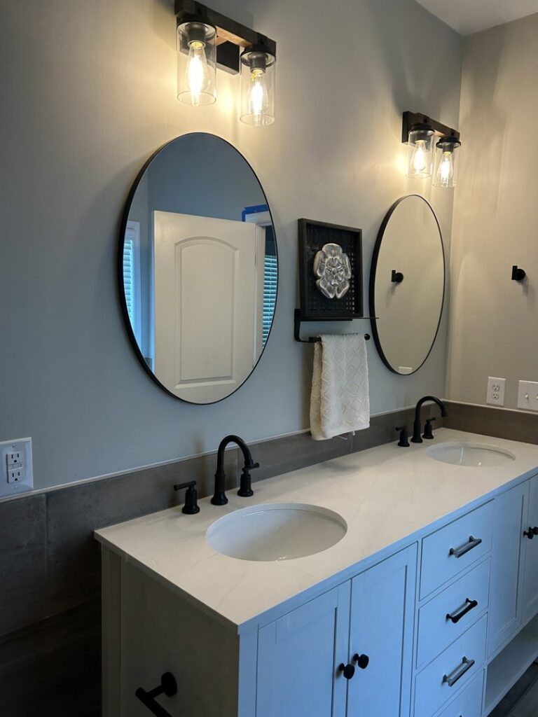 Newly installed bathroom vanity with double sinks, oval mirrors, and modern light fixtures by Supreme Tile & Flooring in Charlotte, NC.