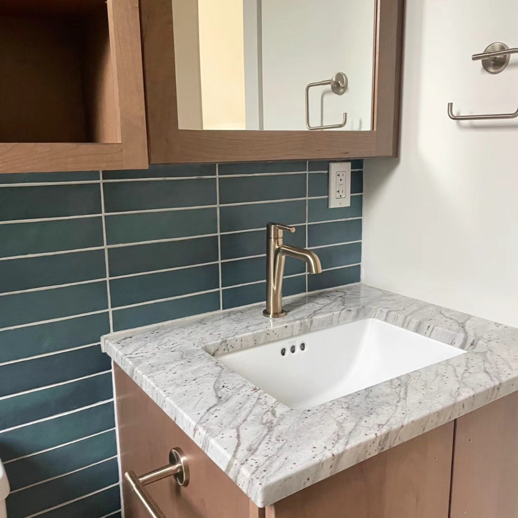 A new bathroom vanity with a granite countertop, gold faucet, and blue tiled backsplash by Buerger Brothers Construction in Lakewood, CO.