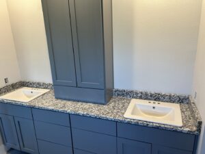 A bathroom vanity with grey cabinets and speckled granite countertops, featuring two sinks, installed by Javier's Countertops in Springdale, AR