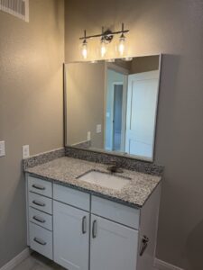A newly installed bathroom vanity with a granite countertop and modern light fixture, a project by Roaring Lion Renovations, LLC in Houston, TX.