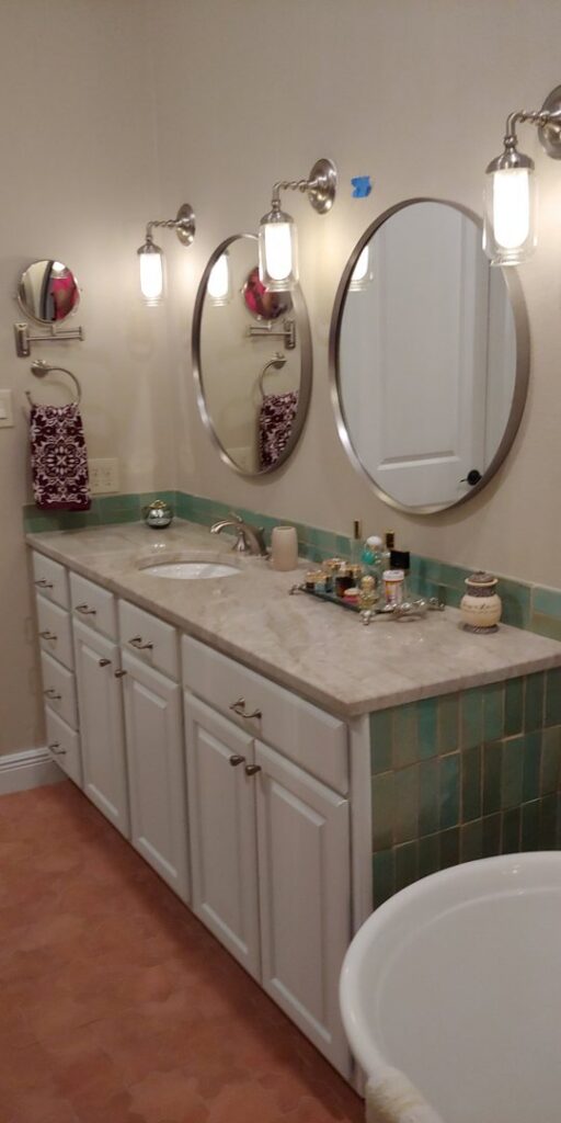 A bathroom vanity installation with white cabinets and green subway tile backsplash by Stone Age Granite of Austin, TX.