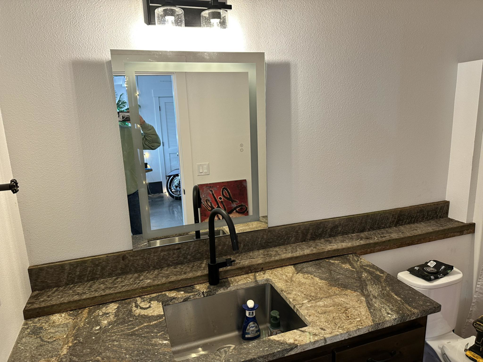 A newly installed bathroom vanity with a modern mirror, faucet, and custom wooden shelf by Valleys Finest Custom Finishes LLC in Salem, OR.