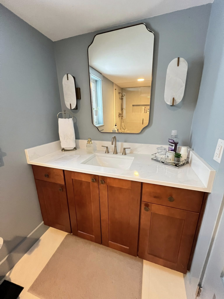 A newly installed bathroom vanity with a wooden cabinet, white countertop, and mirror by Extra Mile Tile in Cincinnati, OH.
