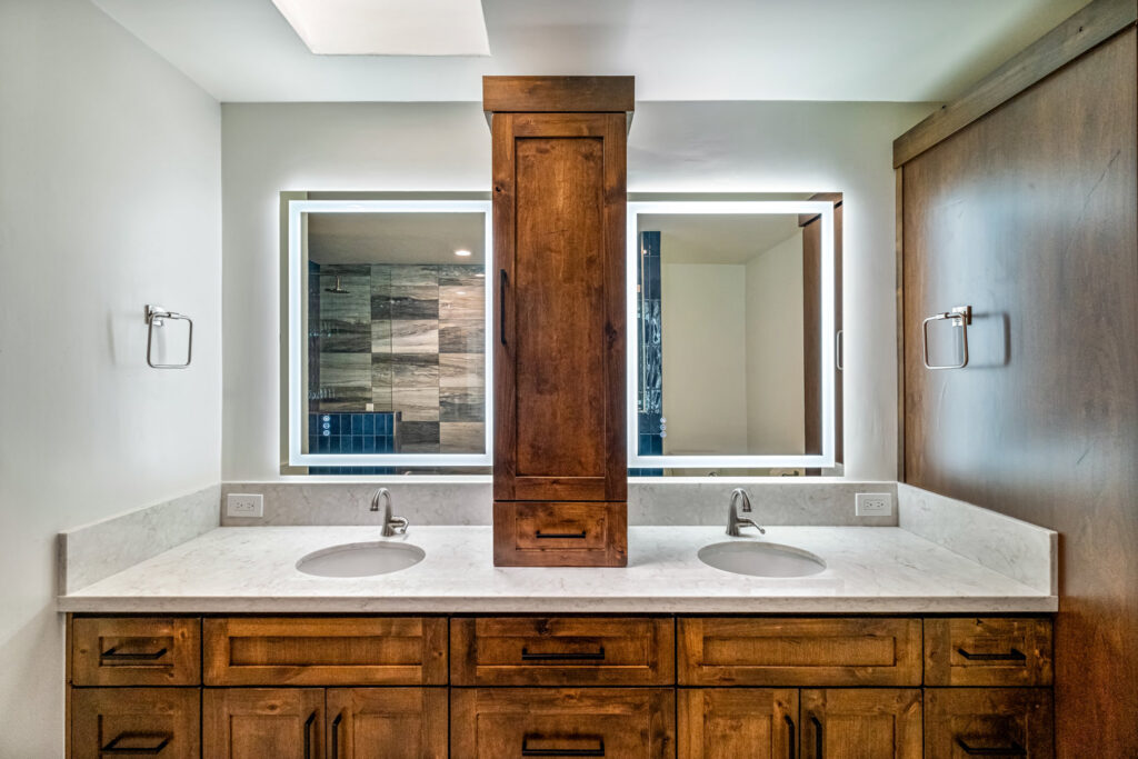 A custom bathroom vanity with double sinks, wooden cabinets, and modern backlit mirrors installed by Ignite Construction in Tempe, AZ.