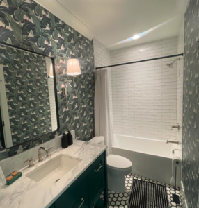 A renovated bathroom featuring a new vanity, mirror, light fixtures, tile, and wallpaper by Ravenel Construction Group in Mount Pleasant, SC