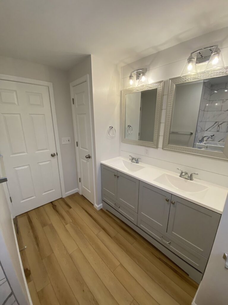 A renovated bathroom featuring a double vanity, modern mirrors, and shiplap wall paneling by Rock Solid Construction in Rochester, NY