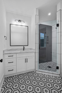 A modern bathroom featuring a white vanity, black mirror, and walk-in shower with hexagonal floor tiles by CML Builders in Charlotte, NC.