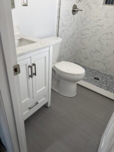 A renovated bathroom with a white vanity, toilet, and tiled shower by M J Services Home Remodeling in Gaithersburg, MD.