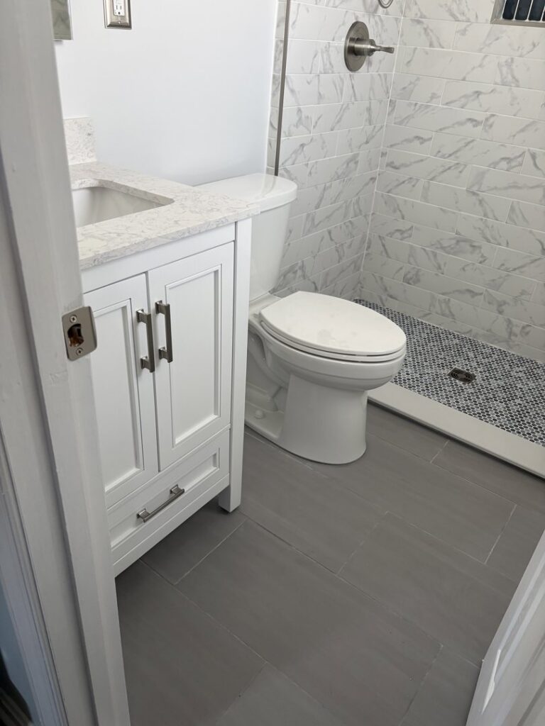 A renovated bathroom with a white vanity, toilet, and tiled shower by M J Services Home Remodeling in Gaithersburg, MD.