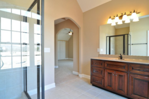 A newly installed bathroom vanity with dark wood cabinets, a sink, mirror, and light fixture, next to a glass shower enclosure by Nixon Construction in Nashville, TN.