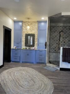 A renovated bathroom featuring a blue vanity, stone accent wall, and modern mirror by Halpin Hands in Williams, OR.