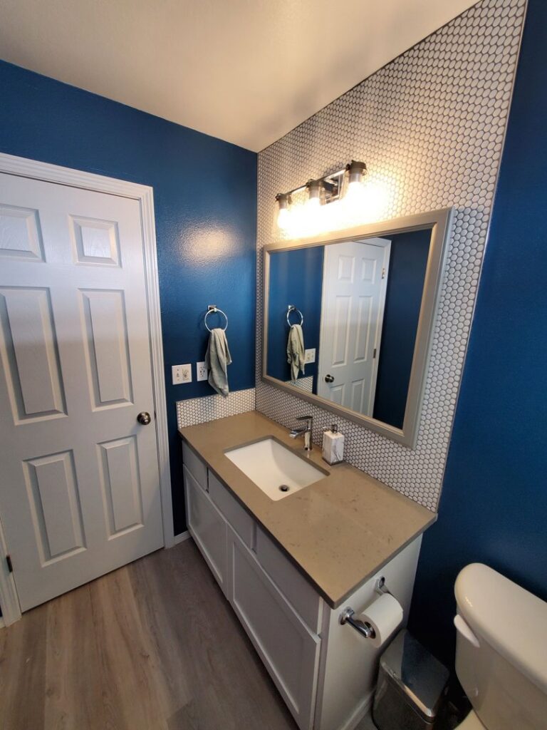 A bathroom vanity with a sink, mirror, and blue walls with a white hexagonal tile backsplash by Myers & Myers Construction in Spokane, WA.