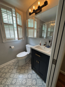 A newly remodeled bathroom featuring a dark vanity, sink, mirror cabinet, toilet, and patterned floor tiles by NC Home Remodeling and Custom Cabinetry in Alexandria, VA.