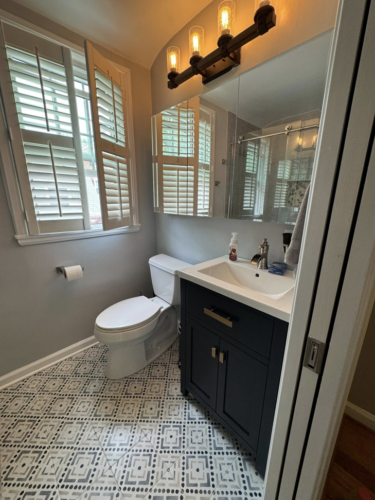 A newly remodeled bathroom featuring a dark vanity, sink, mirror cabinet, toilet, and patterned floor tiles by NC Home Remodeling and Custom Cabinetry in Alexandria, VA.