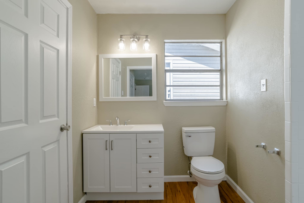 A renovated bathroom featuring a new white vanity, mirror, light fixture, and toilet installed by SSS Solutions, LLC in Mobile, AL.