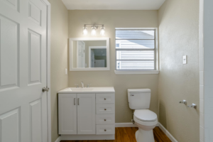 A renovated bathroom featuring a new white vanity, mirror, light fixture, and toilet installed by SSS Solutions, LLC in Mobile, AL.