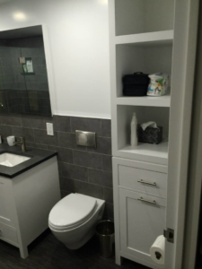 A modern bathroom with a white vanity, wall-mounted toilet, and tall storage cabinet by Executech Interiors in Yonkers, NY