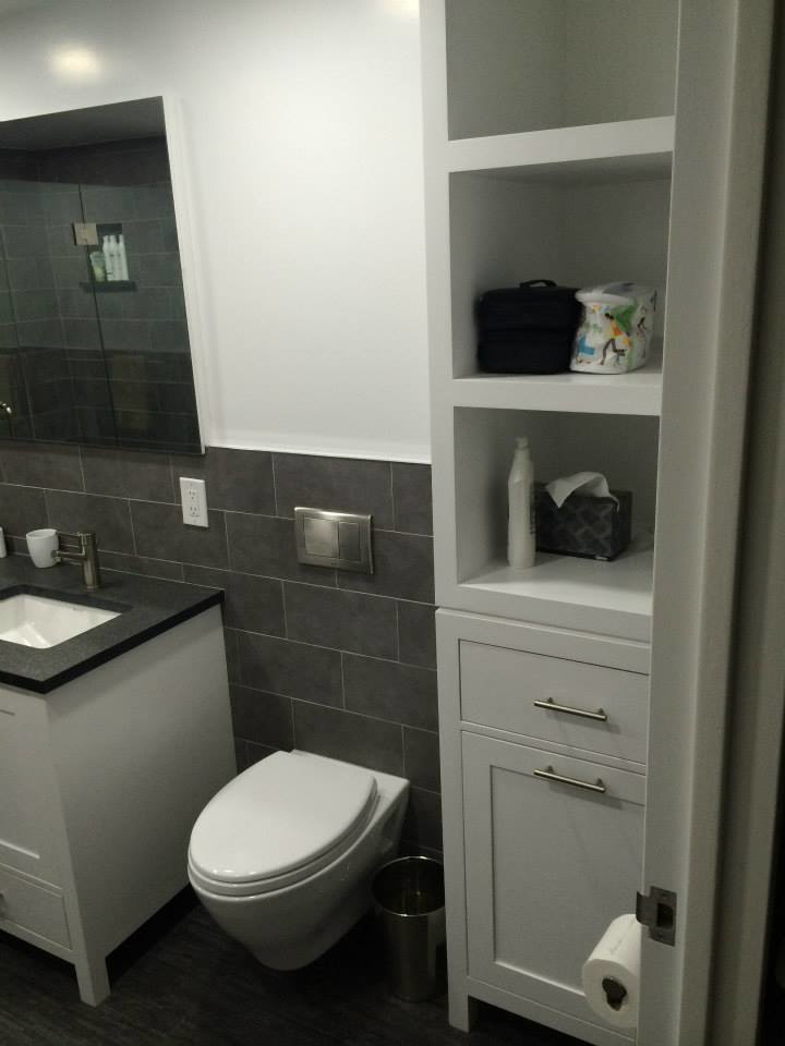 A modern bathroom with a white vanity, wall-mounted toilet, and tall storage cabinet by Executech Interiors in Yonkers, NY