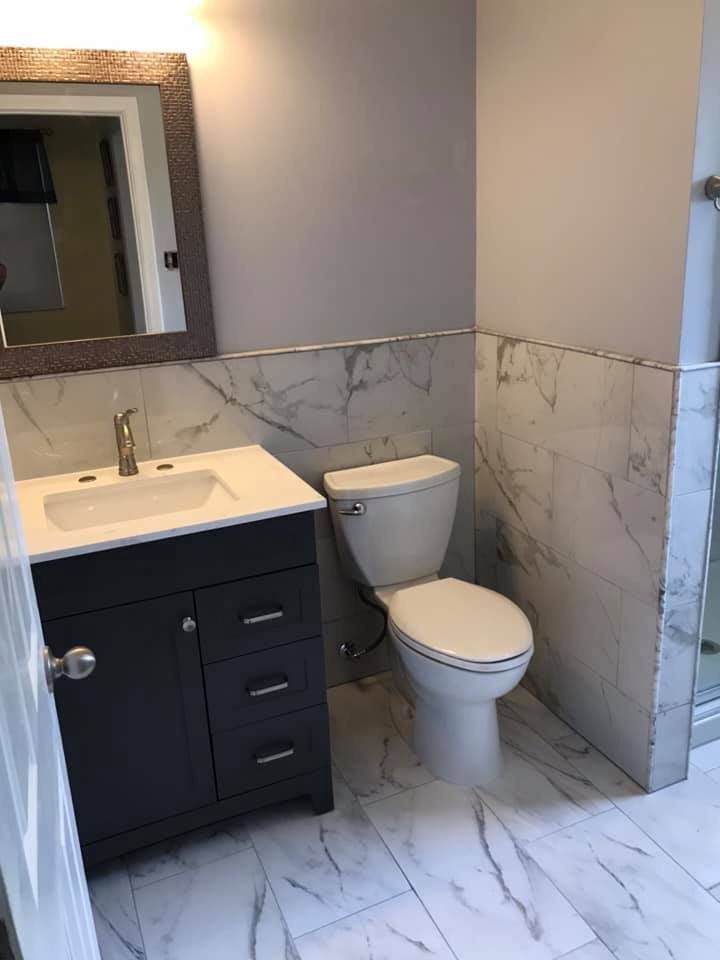 A renovated bathroom with a new vanity, toilet, and marble-look tile on walls and floor by Pro Remodel LLC in St. Charles, MO.
