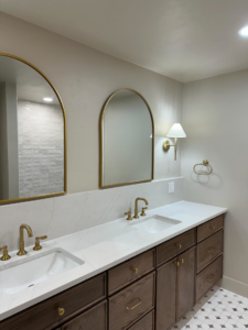 A newly installed bathroom vanity with double sinks, gold faucets, and arched mirrors by Le Roux Homes in Enid, OK.