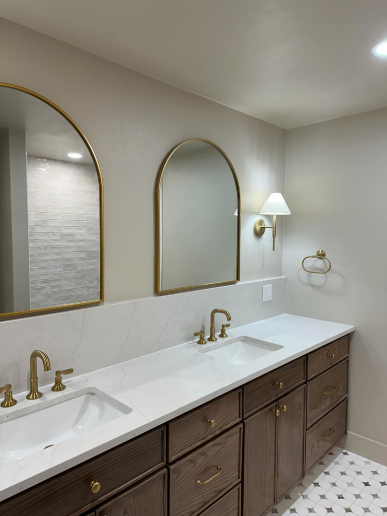 A newly installed bathroom vanity with double sinks, gold faucets, and arched mirrors by Le Roux Homes in Enid, OK.