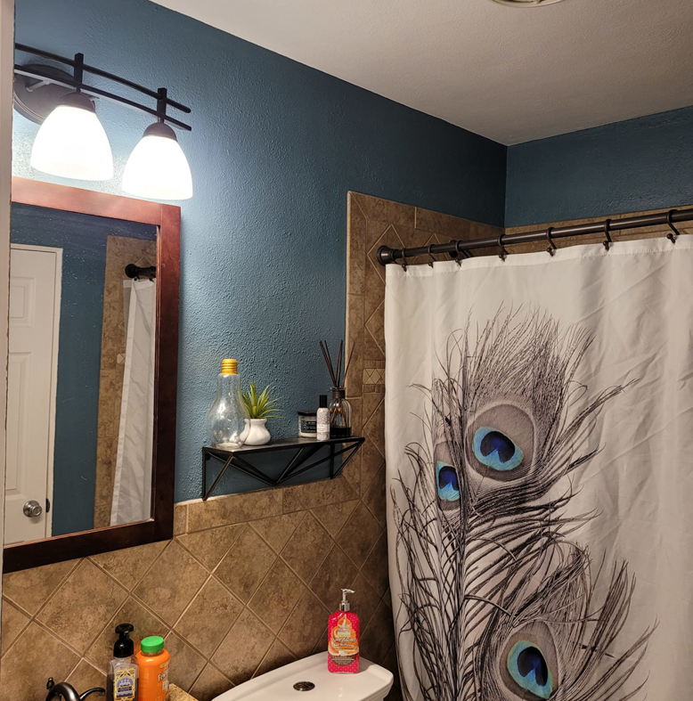 A freshly painted blue bathroom wall with a mirror and light fixture by Logical Drywall and Painting in St. Louis, MO.