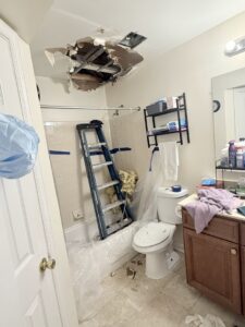 A bathroom showing water damage to the ceiling and a ladder set up for repair work by JF Plumbing & Heating in Rockville, MD.