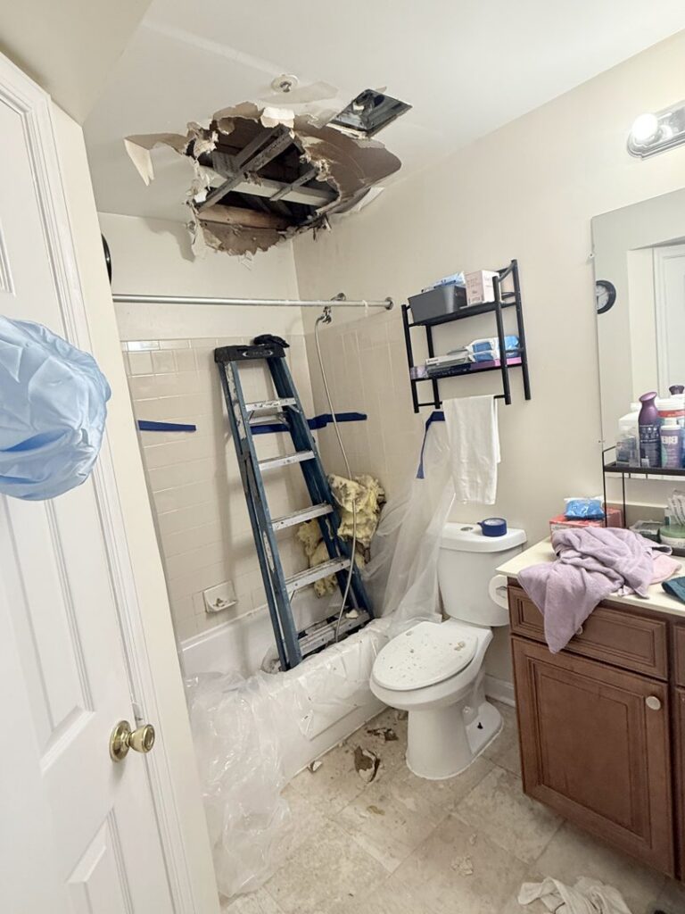 A bathroom showing water damage to the ceiling and a ladder set up for repair work by JF Plumbing & Heating in Rockville, MD.