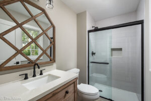 A modern bathroom featuring a wood vanity, black fixtures, and a glass shower, a renovation by Autumn Homes in Naperville, IL.