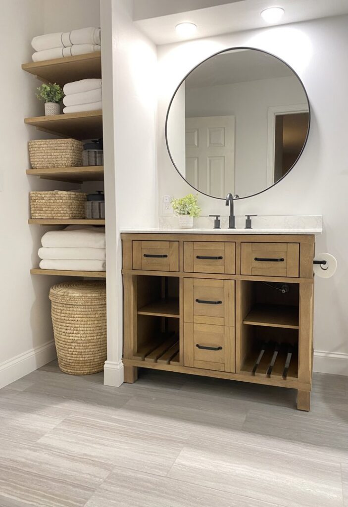 A bathroom featuring a stylish wood vanity with open shelving and a round mirror, installed by Westrick Homes in St. Louis, MO.