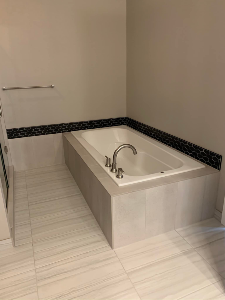 A bathtub installation with a tiled surround and dark accent tiles by Andalex Construction LLC in Gresham, OR.