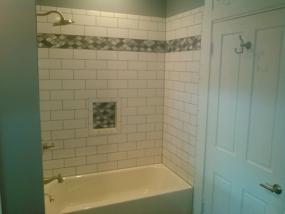 A renovated bathtub and shower combo with white subway tiles and a decorative mosaic band by Paulus Contracting in Fayetteville, OH