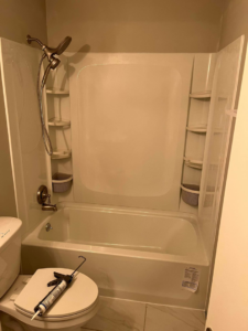 A newly installed bathtub and shower unit with a caulk gun on the toilet, indicating a recent job by JB Recovery in Columbus, OH.
